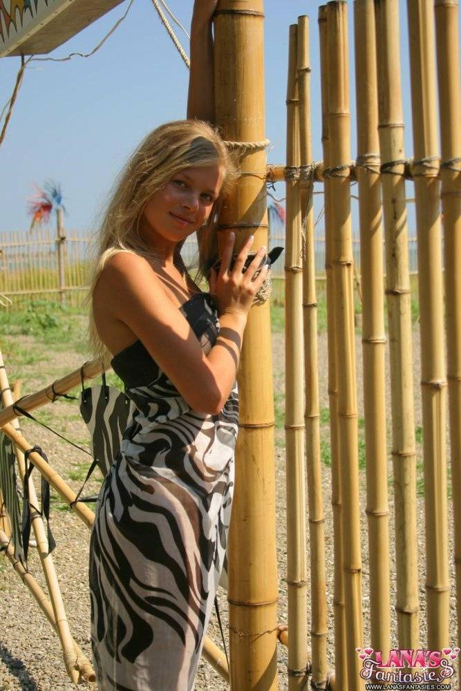 Young blonde girl exposes her thong up against a bamboo fence - #3